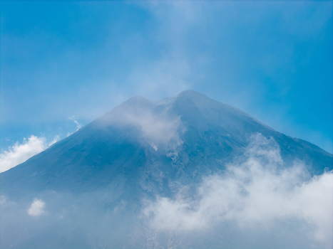 Aerial view of Mount Semeru volcano peak partially covered by clouds under a clear blue sky in Pronojiwo East Java Indonesia.