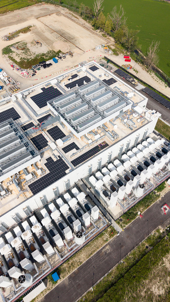Aerial view of a modern hyperscale data center featuring rows of cooling units solar panels on the roof and industrial infrastructure in Melegnano Lombardy Italy.
