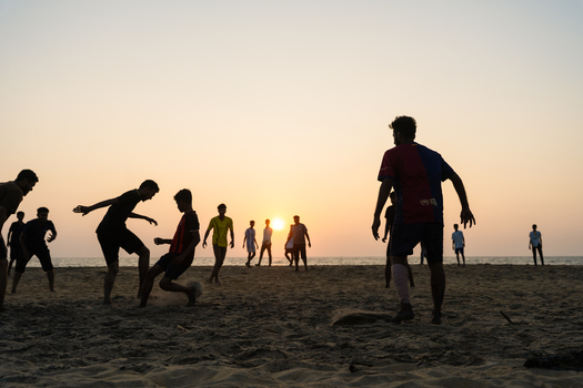 Sri Lanka 23 January 2026 View of young men playing football on a sandy beach at sunset with the sun low on the horizon and the ocean in the background.