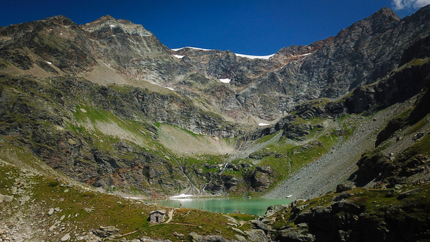 Aerial view of Lago di San Grato s turquoise waters nestled amidst rugged rocky mountain terrain with patches of vibrant green vegetation Valgrisenche Aosta Valley Italy.