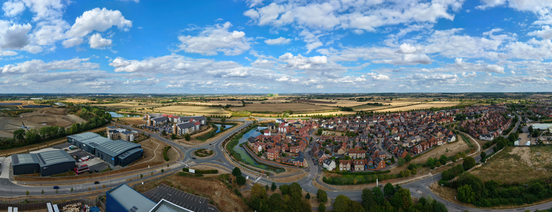 Aerial view of a modern residential housing estate with red brick houses winding roads and green spaces surrounded by open fields in Bedford England United Kingdom. Aerial view of a modern residential housing estate with red brick houses winding roads and green spaces surrounded by open fields in Bedford England United Kingdom.