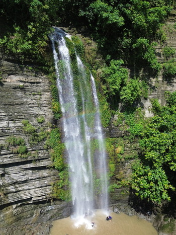 Aerial view of the Sitakund waterfall cascading down a lush rocky cliff face into a pool with people standing at the base in Sitakund Chittagong Division Bangladesh. Aerial view of the Sitakund waterfall cascading down a lush rocky cliff face into a pool with people standing at the base in Sitakund Chittagong Division Bangladesh.