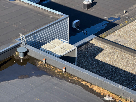 Aerial view of a flat roof featuring HVAC units gravel sections puddles and a small ladder in Leeuwarden Friesland Netherlands.