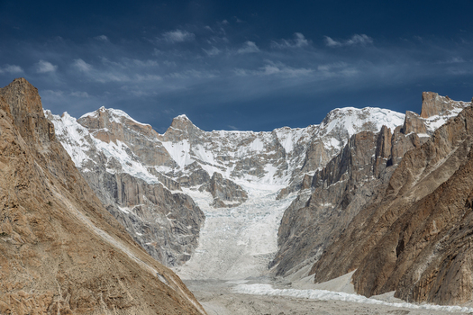 View of Baltoro Glacier with snow capped peaks rugged rocky mountain slopes and glacial ice under a clear blue sky in Baltoro Gilgit Baltistan Pakistan.