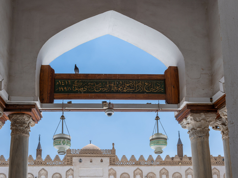 View of Al Azhar Mosque through an ornate archway with marble columns hanging lamps and Arabic calligraphy on a wooden beam in Cairo Egypt. View of Al Azhar Mosque through an ornate archway with marble columns hanging lamps and Arabic calligraphy on a wooden beam in Cairo Egypt.