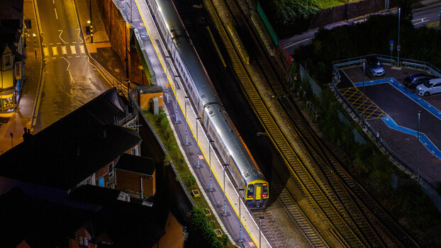 Aerial view of a passenger train stopped at a railway station platform at night with illuminated tracks and surrounding urban infrastructure in Salisbury Wiltshire United Kingdom. Aerial view of a passenger train stopped at a railway station platform at night with illuminated tracks and surrounding urban infrastructure in Salisbury Wiltshire United Kingdom.
