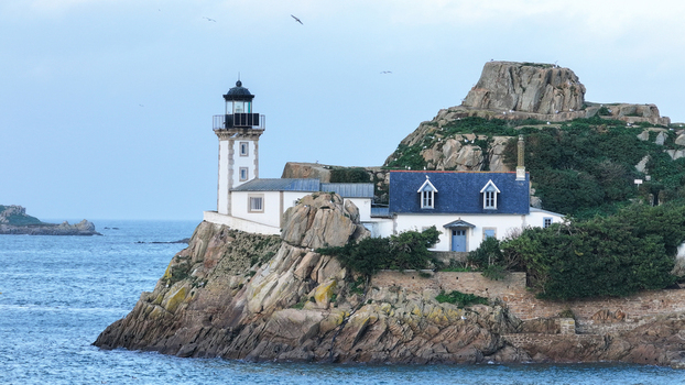 Aerial view of Louet island featuring the historic lighthouse and white cottage perched on rocky cliffs surrounded by the sea in Carantec Brittany France. Aerial view of Louet island featuring the historic lighthouse and white cottage perched on rocky cliffs surrounded by the sea in Carantec Brittany France.