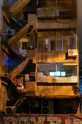 View of an old residential building in Ximen with an external staircase metal security grilles and air conditioning units illuminated at night in Guangfu Village Taipei City Taiwan. View of an old residential building in Ximen with an external staircase metal security grilles and air conditioning units illuminated at night in Guangfu Village Taipei City Taiwan.