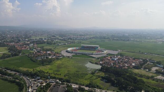 Aerial view of Gelora Bandung Lautan Api Stadium surrounded by green fields residential areas and a road with traffic in Kecamatan Gedebage Jawa Barat Indonesia. Aerial view of Gelora Bandung Lautan Api Stadium surrounded by green fields residential areas and a road with traffic in Kecamatan Gedebage Jawa Barat Indonesia.
