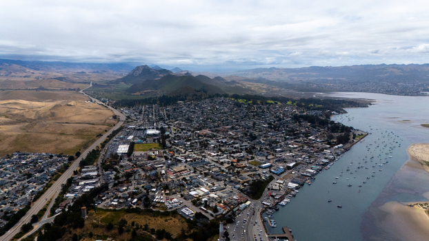Aerial view of the coastal town and harbor with numerous boats featuring the iconic Morro Rock and surrounding hills under a cloudy sky Morro Bay California United States.