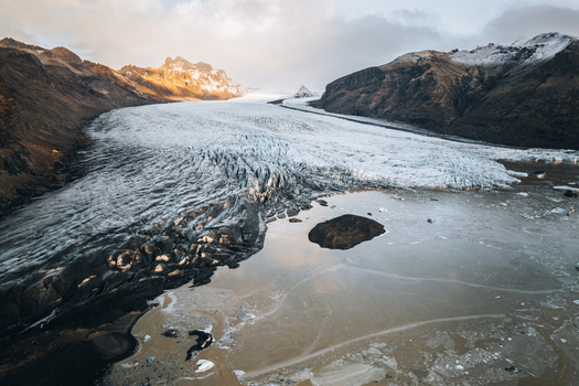 Aerial view of the Skaftafell glacier with its cracked ice surface and rugged mountain peaks under soft sunset light Skaftafell Sveitarfelagid Hornafjordur Iceland. Aerial view of the Skaftafell glacier with its cracked ice surface and rugged mountain peaks under soft sunset light Skaftafell Sveitarfelagid Hornafjordur Iceland.