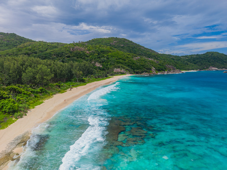 Aerial view of the turquoise waves gently kissing the pristine sands beneath the verdant slopes of Mahe Island Police Bay Mahe Island Seychelles. Aerial view of the turquoise waves gently kissing the pristine sands beneath the verdant slopes of Mahe Island Police Bay Mahe Island Seychelles.
