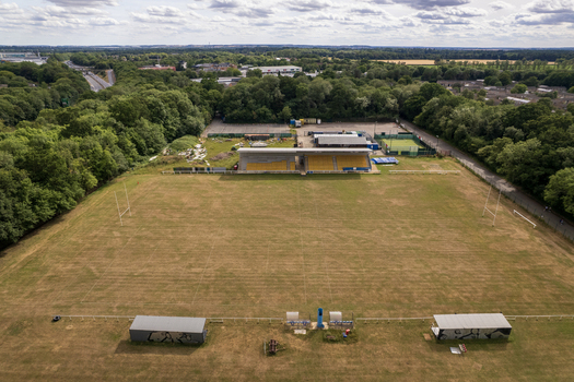 Aerial view of Bretton Park sports field featuring a rugby pitch with a small grandstand surrounded by lush green trees and parkland in Peterborough England United Kingdom. Aerial view of Bretton Park sports field featuring a rugby pitch with a small grandstand surrounded by lush green trees and parkland in Peterborough England United Kingdom.
