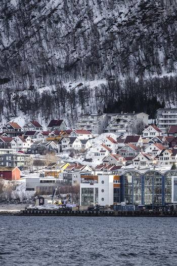 View of the colorful residential houses and modern waterfront buildings nestled at the foot of a snowy mountain in Tromso Troms Norway.