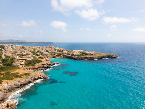 Aerial view of the turquoise coastline and rocky cliffs with residential buildings and lush vegetation under a bright sky in Sa Coma Balearic Islands Spain. Aerial view of the turquoise coastline and rocky cliffs with residential buildings and lush vegetation under a bright sky in Sa Coma Balearic Islands Spain.
