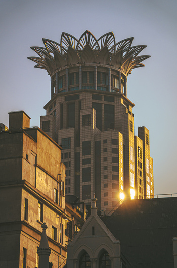 View of the distinctive crown like architecture of a skyscraper at The Bund illuminated by golden hour sunlight with historic building rooftops in the foreground Shanghai Shanghai China.