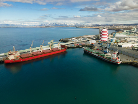 Hafnarfjordur Iceland 17 April 2026 Aerial view of the industrial port with large cargo ships docked at the pier featuring a striped silo and snow capped mountains in the background. Hafnarfjordur Iceland 17 April 2026 Aerial view of the industrial port with large cargo ships docked at the pier featuring a striped silo and snow capped mountains in the background.