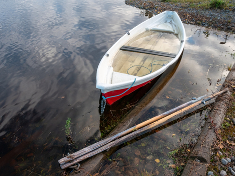 View of a row boat partially submerged in river water after a flood with wooden oars resting on the muddy bank in Muhos North Ostrobothnia Finland.