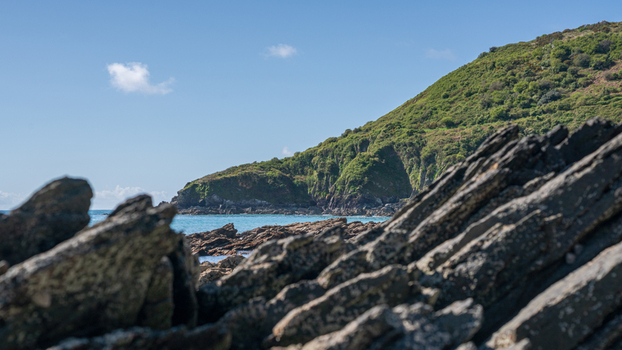 View of the rugged coastline along the South West Coastal Path overlooking Portnadler Bay with dark rocks and green hills under a clear blue sky in Looe Cornwall United Kingdom. View of the rugged coastline along the South West Coastal Path overlooking Portnadler Bay with dark rocks and green hills under a clear blue sky in Looe Cornwall United Kingdom.