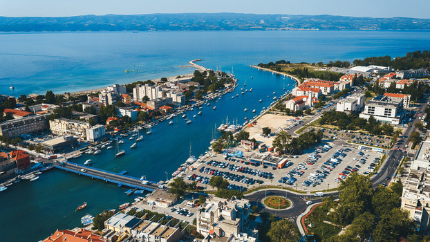 Aerial view of the Cetina River mouth in Omis featuring a bridge boats moored in the water a parking area and urban architecture in Split Dalmatia County Croatia. Aerial view of the Cetina River mouth in Omis featuring a bridge boats moored in the water a parking area and urban architecture in Split Dalmatia County Croatia.