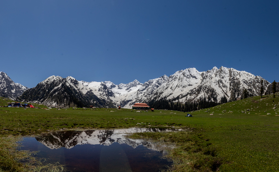 View of Jahaz Banda Alpine Rest House nestled in the green meadows of Kumrat Valley with snow capped mountains reflecting in a pond Kumrat Valley Khyber Pakhtunkhwa Pakistan. View of Jahaz Banda Alpine Rest House nestled in the green meadows of Kumrat Valley with snow capped mountains reflecting in a pond Kumrat Valley Khyber Pakhtunkhwa Pakistan.