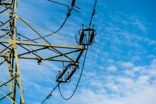 View of a high voltage electricity pylon with insulators and power lines against a clear blue sky in Poland.