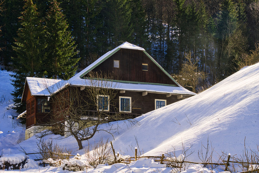 View of a rustic dark wooden cabin nestled in the snow covered landscape beneath towering evergreen trees offering a tranquil winter scene Moce Slovakia.