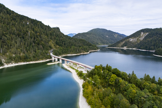 Aerial view of the bridge spanning the Sylvensteinsee with its turquoise waters reflecting the forested hills under a vast sky Sylvensteinspeicher Bavaria Germany. Aerial view of the bridge spanning the Sylvensteinsee with its turquoise waters reflecting the forested hills under a vast sky Sylvensteinspeicher Bavaria Germany.