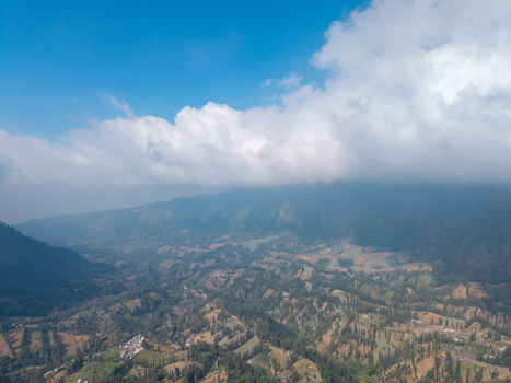 Aerial view of the lush green mountainous landscape of Wonokerto with dense vegetation and clouds over the peaks in Sukorejo East Java Indonesia. Aerial view of the lush green mountainous landscape of Wonokerto with dense vegetation and clouds over the peaks in Sukorejo East Java Indonesia.