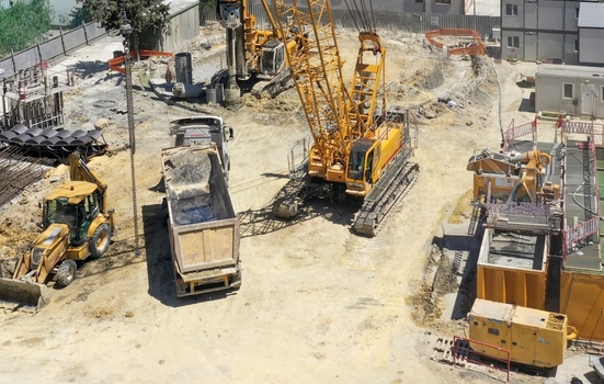 Aerial view of heavy machinery including a yellow crane excavator and dump truck operating on a dusty construction site under bright sunlight Avcilar Istanbul Turkiye. Aerial view of heavy machinery including a yellow crane excavator and dump truck operating on a dusty construction site under bright sunlight Avcilar Istanbul Turkiye.