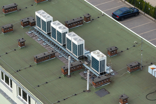 Aerial view of modern HVAC air conditioning units installed on a green rooftop with brick chimneys and a parked car visible below in Warsaw Masovian Voivodeship Poland. Aerial view of modern HVAC air conditioning units installed on a green rooftop with brick chimneys and a parked car visible below in Warsaw Masovian Voivodeship Poland.