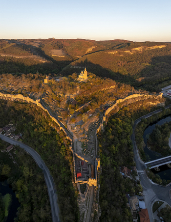 Aerial view of Tsarevets Fortress illuminated by golden hour light featuring historic stone walls the central church and surrounding hills in Veliko Tarnovo Veliko Tarnovo Bulgaria. Aerial view of Tsarevets Fortress illuminated by golden hour light featuring historic stone walls the central church and surrounding hills in Veliko Tarnovo Veliko Tarnovo Bulgaria.