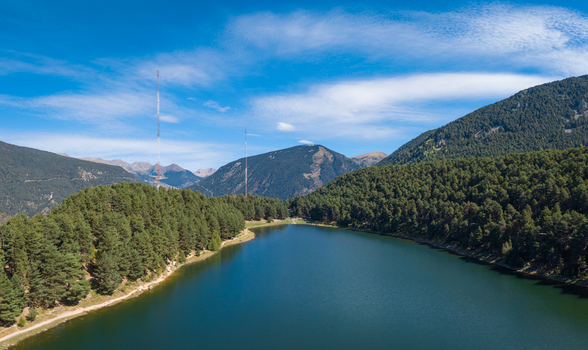 Aerial view of Lake Engolasters surrounded by dense pine forests and rugged mountains under a clear blue sky in Encamp Andorra. Aerial view of Lake Engolasters surrounded by dense pine forests and rugged mountains under a clear blue sky in Encamp Andorra.