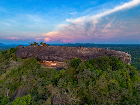 Aerial view of Pidurangala Rock surrounded by lush green jungle under a vibrant sunset sky with people standing on the summit in Sigiriya Central Province Sri Lanka. Aerial view of Pidurangala Rock surrounded by lush green jungle under a vibrant sunset sky with people standing on the summit in Sigiriya Central Province Sri Lanka.
