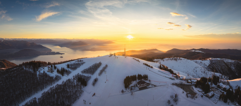 Aerial view of Mottarone mountain covered in snow at sunrise with Lake Maggiore in the background in Stresa Piedmont Italy. Aerial view of Mottarone mountain covered in snow at sunrise with Lake Maggiore in the background in Stresa Piedmont Italy.