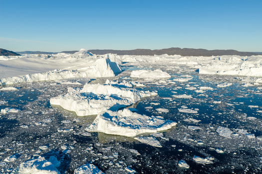 Aerial view of Ilulissat glacier with massive icebergs floating in the deep blue sea under a clear sky in Greenland. Aerial view of Ilulissat glacier with massive icebergs floating in the deep blue sea under a clear sky in Greenland.