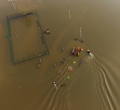 Aerial view of a flooded playground and sports court submerged under murky brown water with a small boat navigating through the area in Kedainiai Kaunas County Lithuania. Aerial view of a flooded playground and sports court submerged under murky brown water with a small boat navigating through the area in Kedainiai Kaunas County Lithuania.