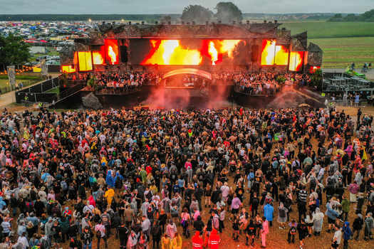 Herzogenaurach Germany 26 July 2025 Aerial view of the Open Beatz Festival main stage with pyrotechnics and a massive crowd of people dancing in a rural field under an overcast sky.