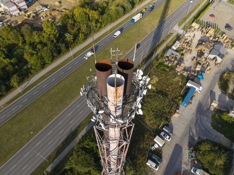 Aerial view of a tall industrial chimney equipped with numerous communication antennas situated near a busy highway and industrial storage area in Poland. Aerial view of a tall industrial chimney equipped with numerous communication antennas situated near a busy highway and industrial storage area in Poland.