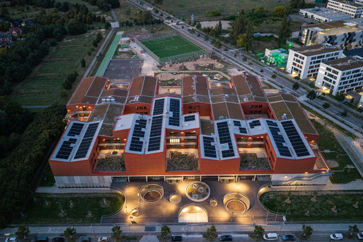 Berlin Germany 07 September 2026 Aerial view of the New School Campus in Adlershof featuring a modern red brick building with solar panels green roofs and illuminated courtyards.
