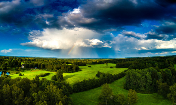 Aerial view of a lush green landscape featuring rolling fields dense forests and a dramatic sky with a rainbow emerging from storm clouds Latvia. Aerial view of a lush green landscape featuring rolling fields dense forests and a dramatic sky with a rainbow emerging from storm clouds Latvia.