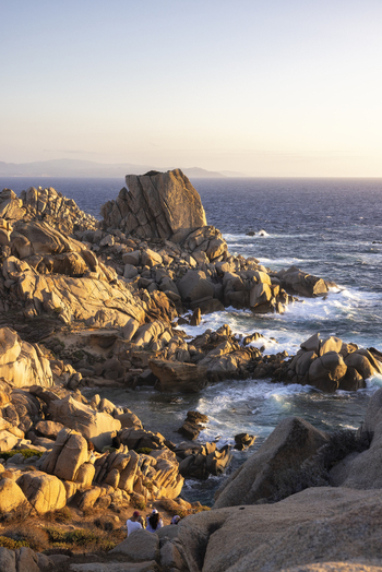 View of the granite rock formations and the blue sea with people sitting on the cliffs during golden hour Capo Testa Sardegna Italy. View of the granite rock formations and the blue sea with people sitting on the cliffs during golden hour Capo Testa Sardegna Italy.