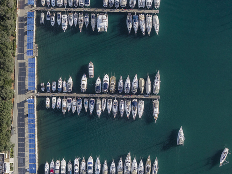 Aerial view of numerous sailboats and yachts moored in the marina surrounded by clear turquoise water and a coastal road with lush trees in Pjescana Uvala Istria Croatia.