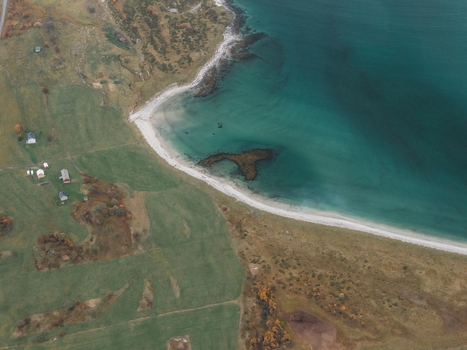 Aerial view of the Lofoten coastline featuring a sandy beach turquoise waters and green fields with scattered houses in Svolvaer Nordland Norway.
