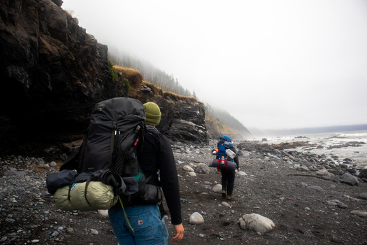 View of hikers with large backpacks walking along the rugged pebble beach of the Lost Coast under a misty sky Humboldt County California United States.
