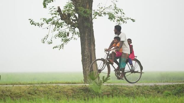 View of a man riding a bicycle with children in Bogura Bangladesh.