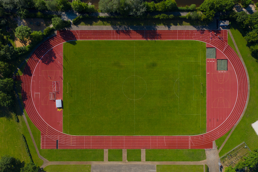 Aerial view of the Sportinsel Forchheim sports facility featuring a green soccer pitch and red running track surrounded by lush trees in Forchheim Bayern Germany.