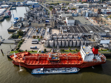Aerial view of a large red tanker ship docked at the industrial port facilities with storage tanks and a smaller barge alongside in Hamburg Germany.
