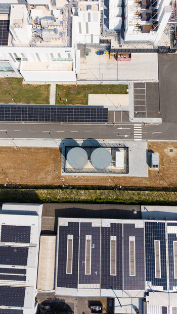 Aerial view of a modern hyperscale data center featuring large industrial buildings with extensive rooftop solar panel arrays cooling tanks and paved service areas Melegnano Lombardy Italy.