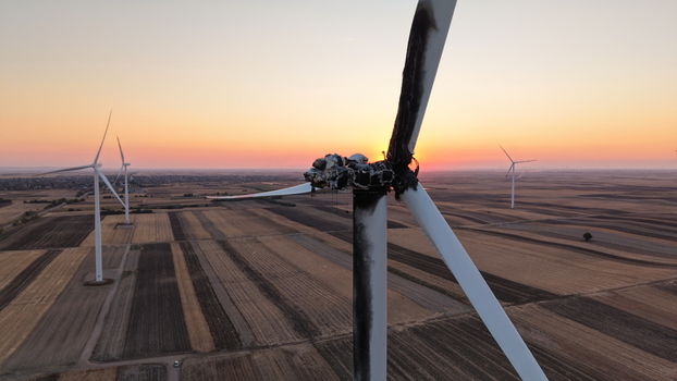 Aerial view of a damaged wind turbine with charred blades and nacelle standing in a vast agricultural field during sunset in Vladimirovac Vojvodina Serbia.